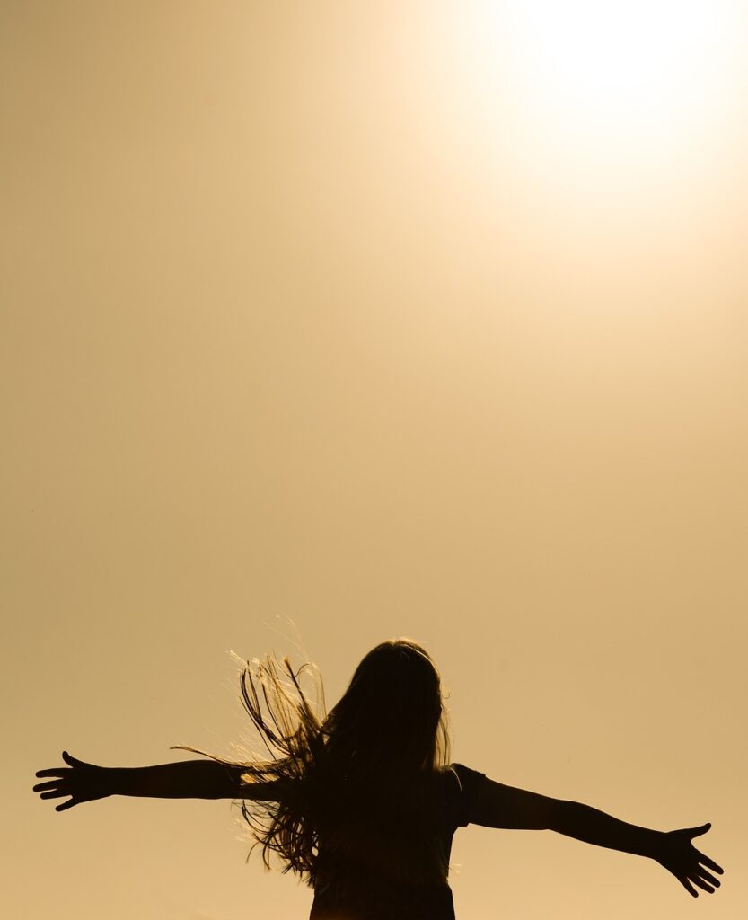 A woman with improved Spiritual, Emotional and Physical Health through Christian Meditation, meditating on the bible and prayer. She hands her arms stretched wide in worship and in awe of the presence of God and gratitude for him in the sunlight. 