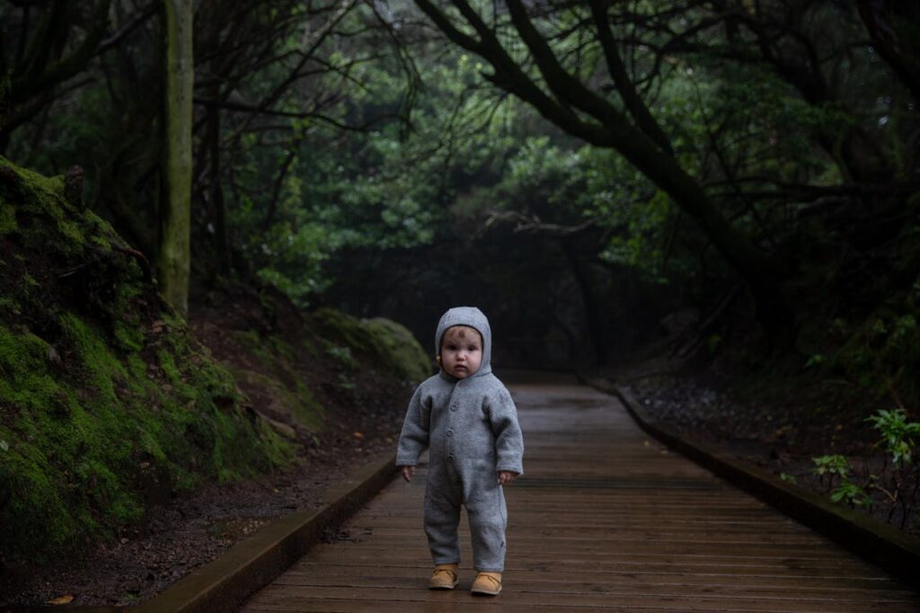 Image used for christian meditation for beginners. Photo of a little boy standing alone on a wooden foot path in the bush wearing a grey onesie looking at you